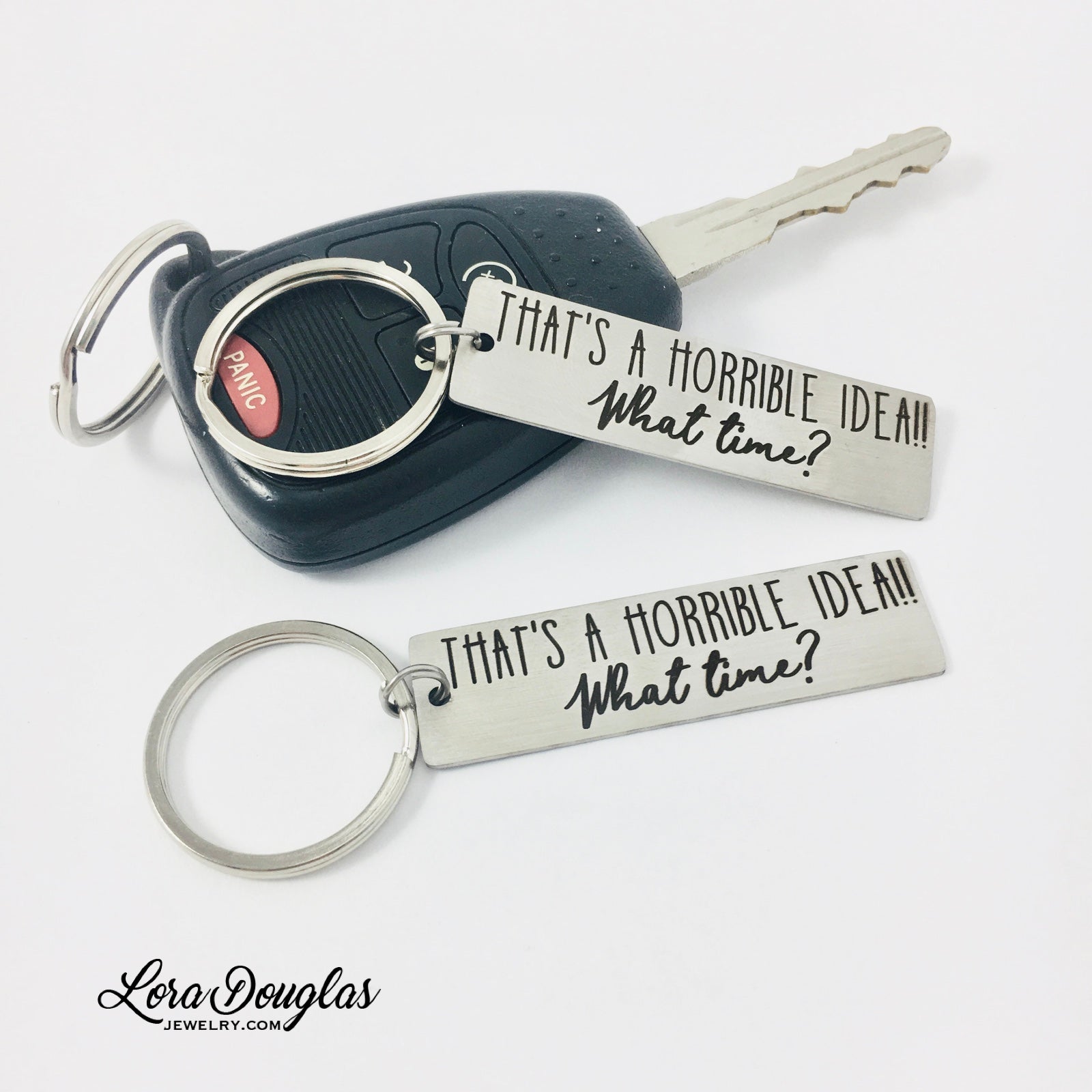 silver stainless steel keychain with black engraving, 'That's a horrible idea! What time?'  Both keychains have a key ring and are displayed on a car key.