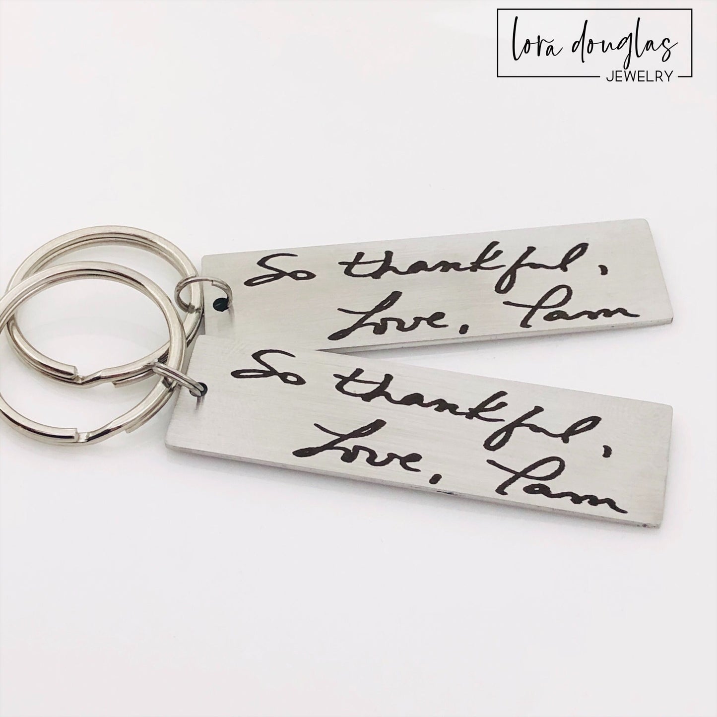 A stainless steel keychain with engraved handwriting samples. The keychain features a silver-colored plate with the text 'I love you dad' and 'Mom you're the best' alongside a standard key ring.