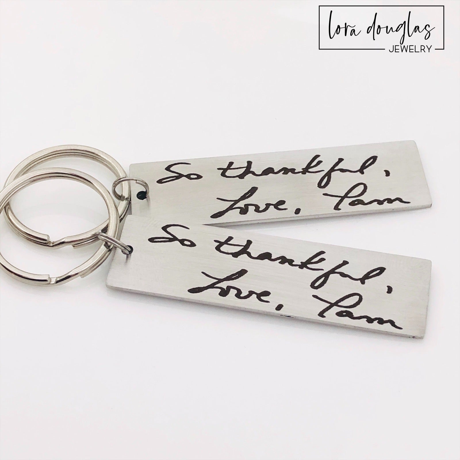 A stainless steel keychain with engraved handwriting samples. The keychain features a silver-colored plate with the text 'I love you dad' and 'Mom you're the best' alongside a standard key ring.