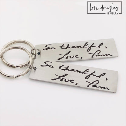 A stainless steel keychain with engraved handwriting samples. The keychain features a silver-colored plate with the text 'I love you dad' and 'Mom you're the best' alongside a standard key ring.