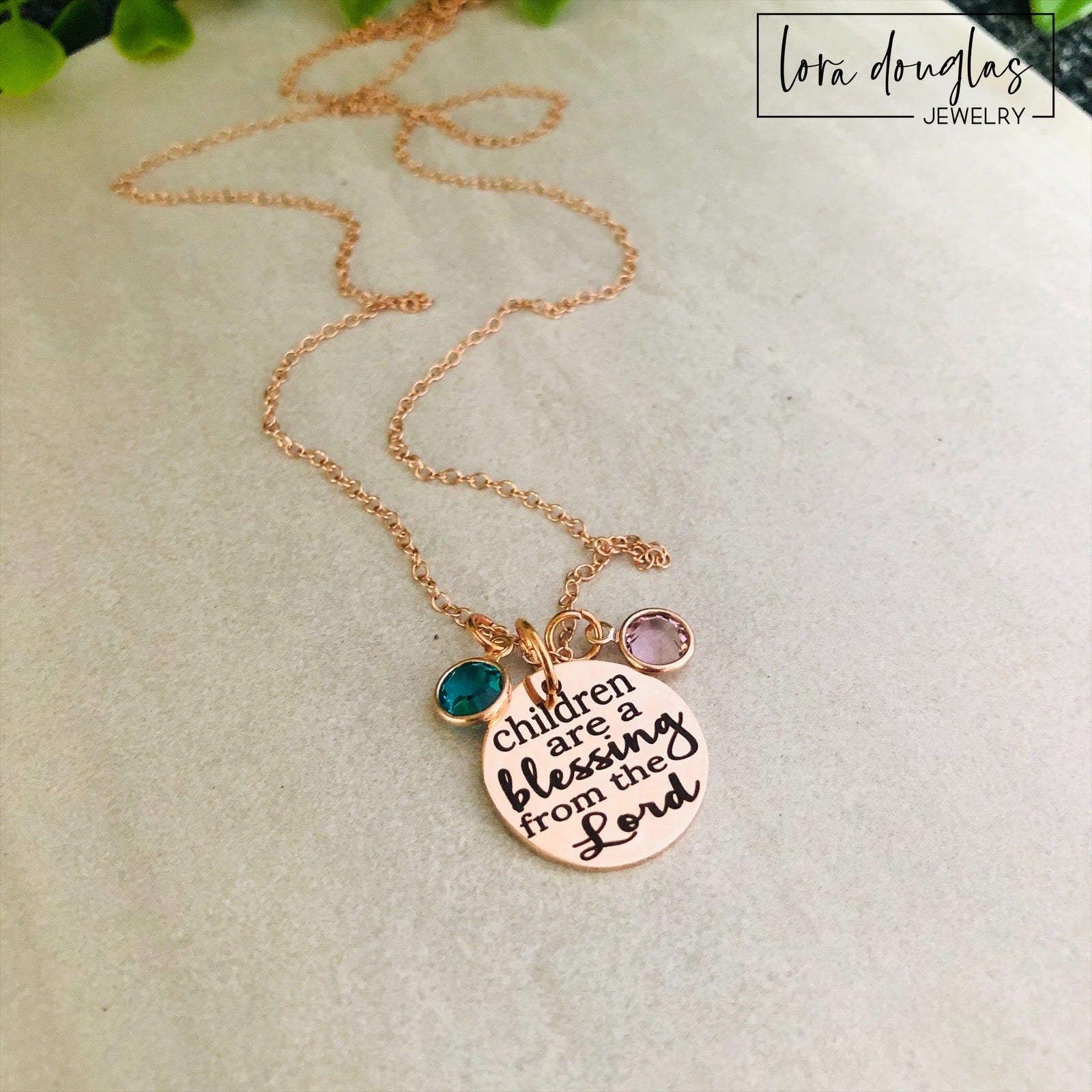 A rose gold stainless steel necklace with a round pendant that has the text 'CHILDREN ARE A BLESSING FROM THE LORD' engraved on it, along with a Swarovski Channel Plated Birthstone Charm.
