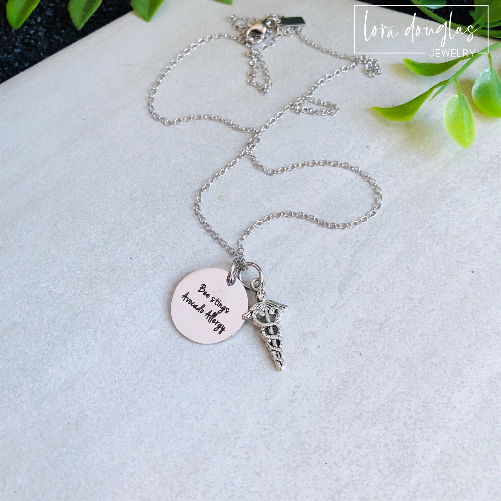 A stainless steel medical alert necklace with a round pendant displaying medical information and a 24-inch chain.