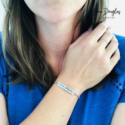 A silver bracelet with a bar pendant engraved with the handwritten message 