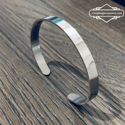 A stainless steel cuff bracelet with a secret message engraved on the inside, against the skin. The bracelet is blank on the outside.