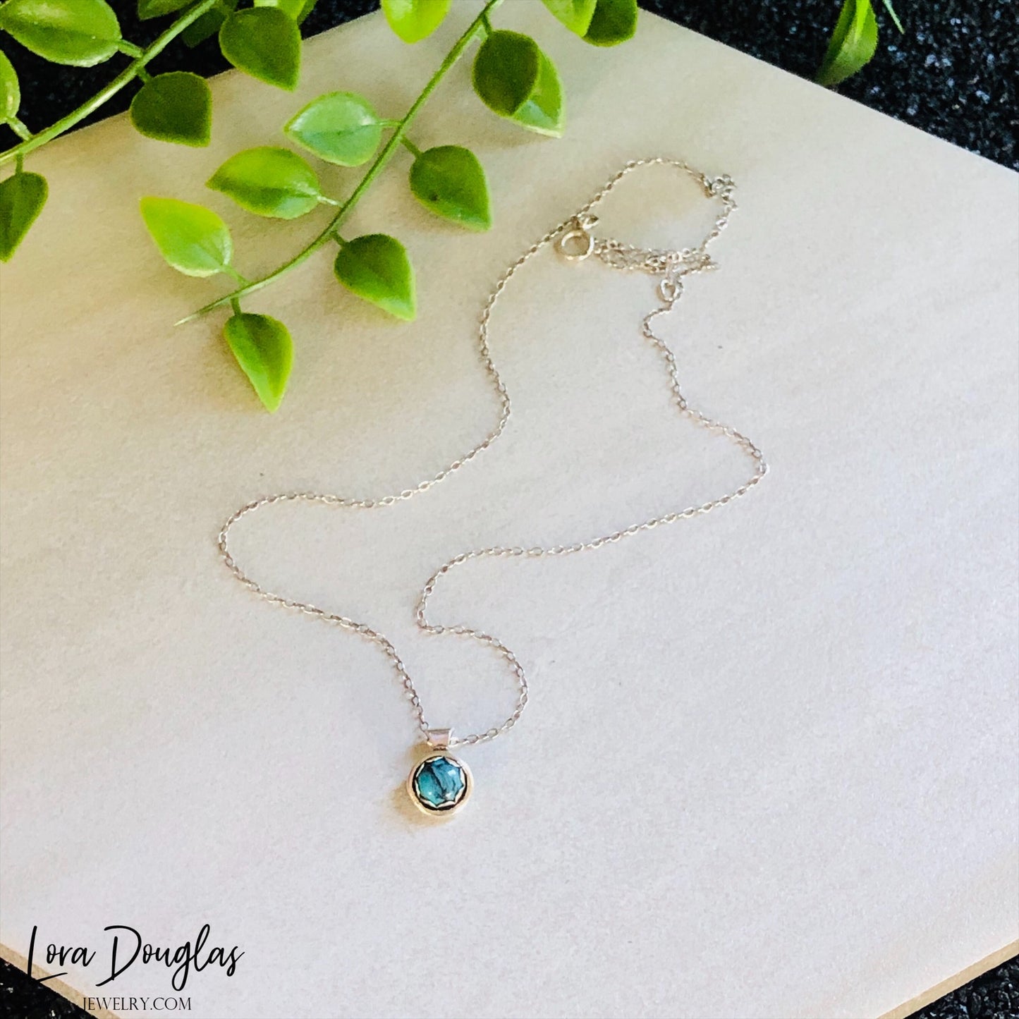 A sterling silver pendant necklace with a turquoise stone, displayed on a silver chain.