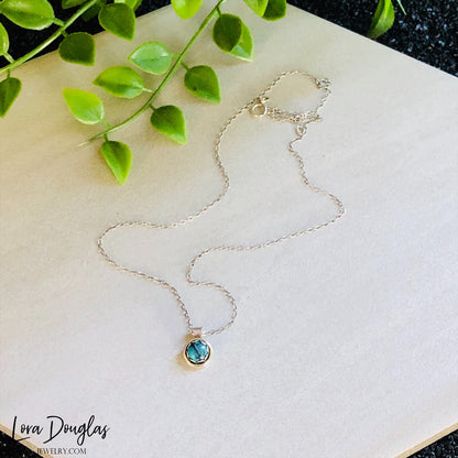 A sterling silver pendant necklace with a turquoise stone, displayed on a silver chain.