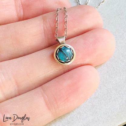 A sterling silver pendant necklace with a turquoise stone, displayed on a silver chain.