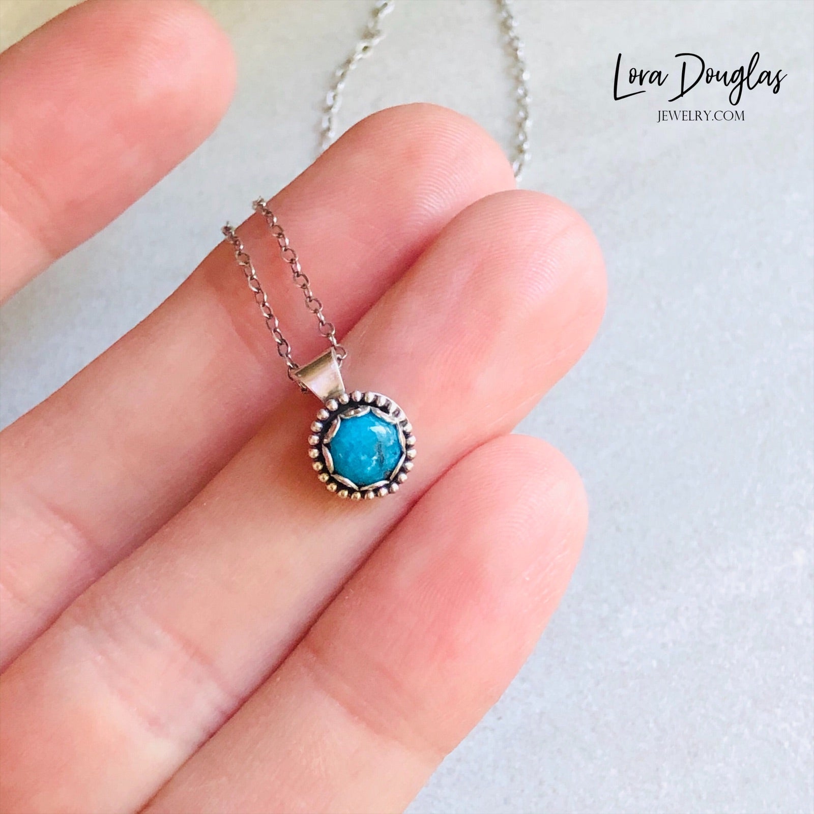 A sterling silver pendant necklace with a turquoise stone, displayed on a silver chain.