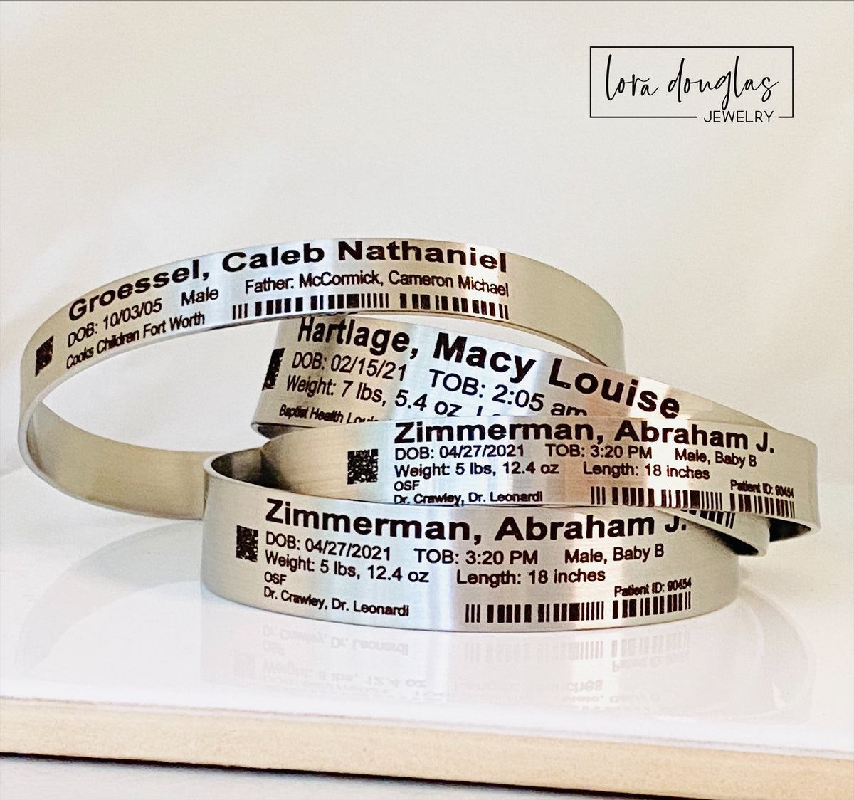 Silver stainless steel baby hospital ID bracelet personalized with a newborn's name, birth date, doctor, hospital and patient information, designed to resemble the identification bracelet received during a hospital birth.
