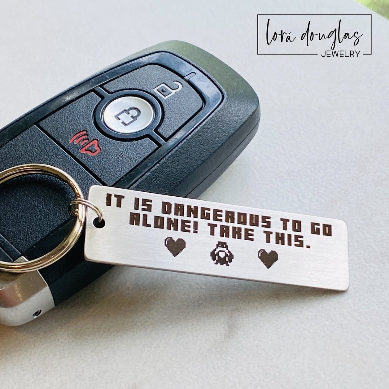 Legend of Zelda inspired keychain engraved with the iconic "It is dangerous to go alone. Take this." quote and two pixel hearts on a stainless steel rectangle keychain. Optional personalized engraving on the back makes this a meaningful gamer gift for anniversaries, Valentine's Day, or your player two.
