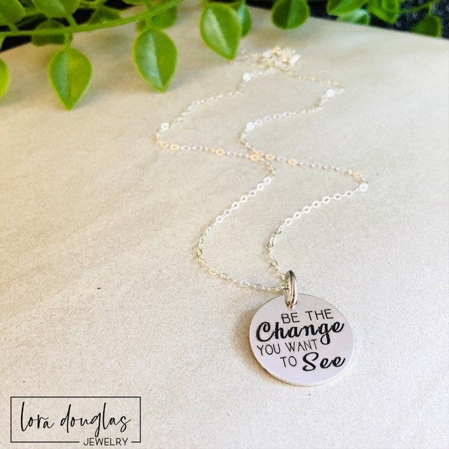 be the change you want to see necklace with 3/4 inch round engraved charm in stainless steel gold or silver finish displayed on chain highlighting minimal design and inspirational message jewelry