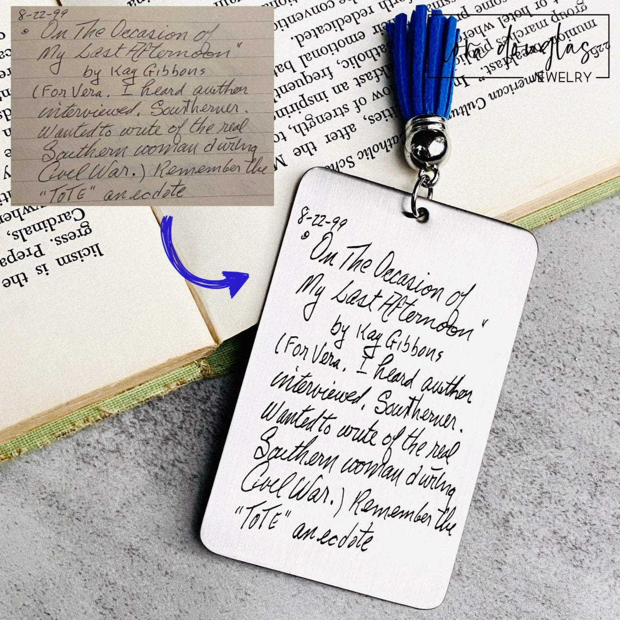 A custom engraved bookmark with a personal message, displayed on an open book. The bookmark is silver with black engraving and has a navy blue velvet drawstring pouch with a gift tag.