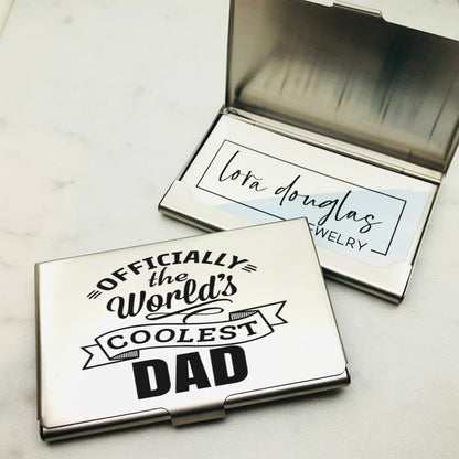 A stainless steel business card holder with the engraving 'OFFICIALLY THE WORLD'S COOLEST DAD' on the front cover, alongside a closed case.