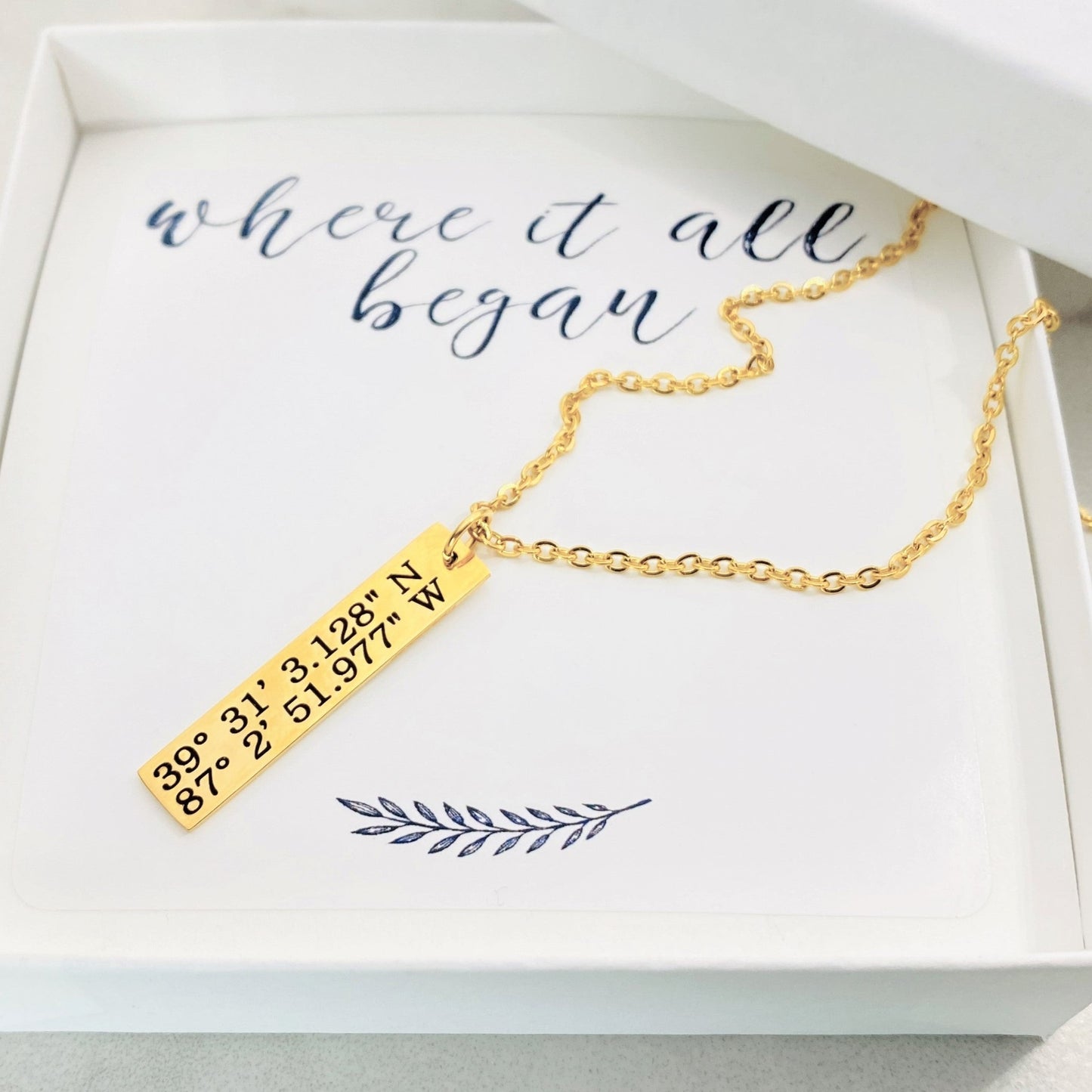 gold necklace engraved with latitude and longitude coordinates in a box that says where it all began
