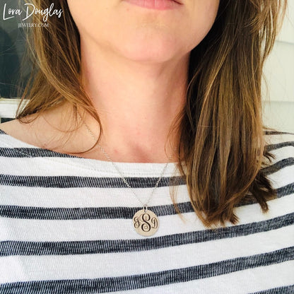 A silver monogram necklace with an engraved initial pendant laid out on a marble surface.