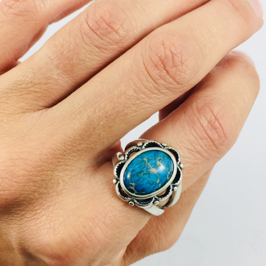 A sterling silver ring with a blue sea sediment jasper gemstone, placed on a white surface.