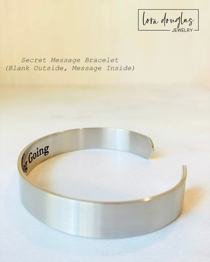 A stainless steel cuff bracelet with a secret message engraved on the inside, against the skin. The bracelet is blank on the outside.