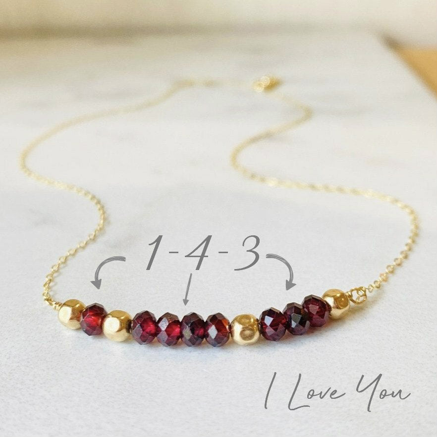 A garnet and gold-filled necklace with a meaningful inscription '1-4-3 I LOVE YOU' displayed on a card.