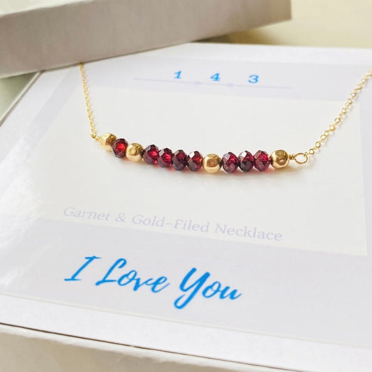 A garnet and gold-filled necklace with a meaningful inscription '1-4-3 I LOVE YOU' displayed on a card.
