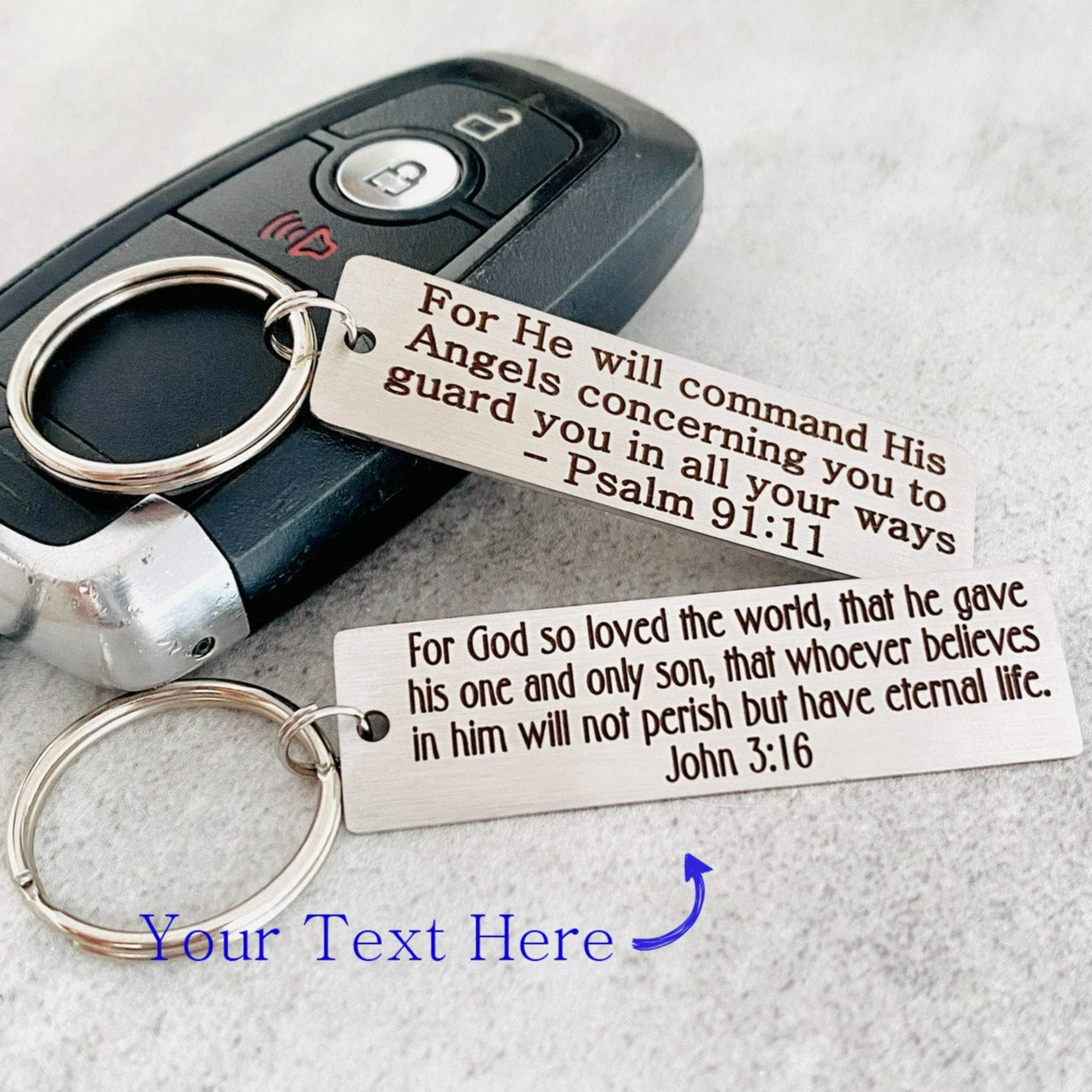Two metal keychains with Bible verses engraved on them, placed on a car key.