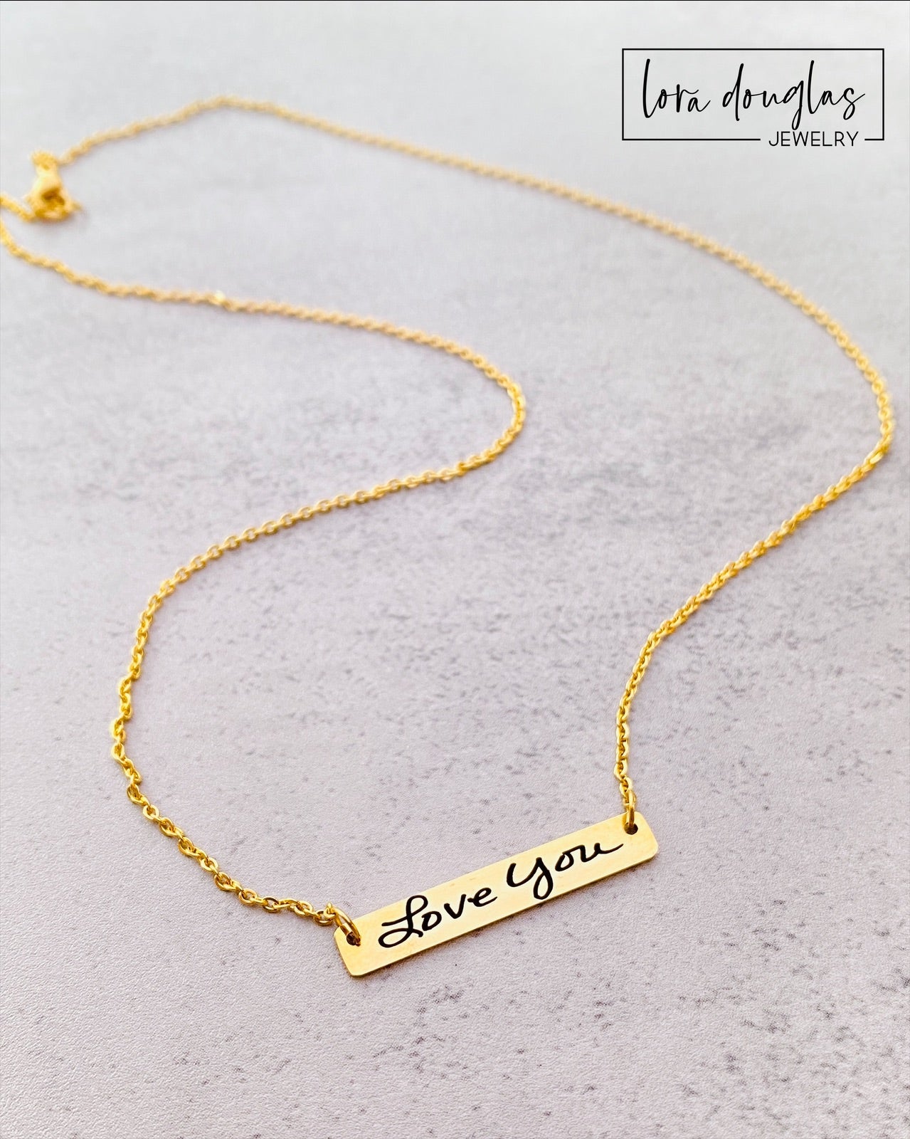 A gold bar necklace with engraved handwriting on it