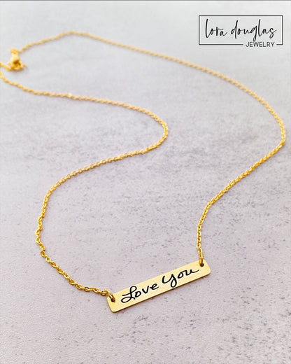 A gold bar necklace with engraved handwriting on it