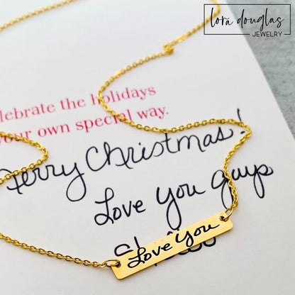 A gold bar necklace with engraved handwriting on it