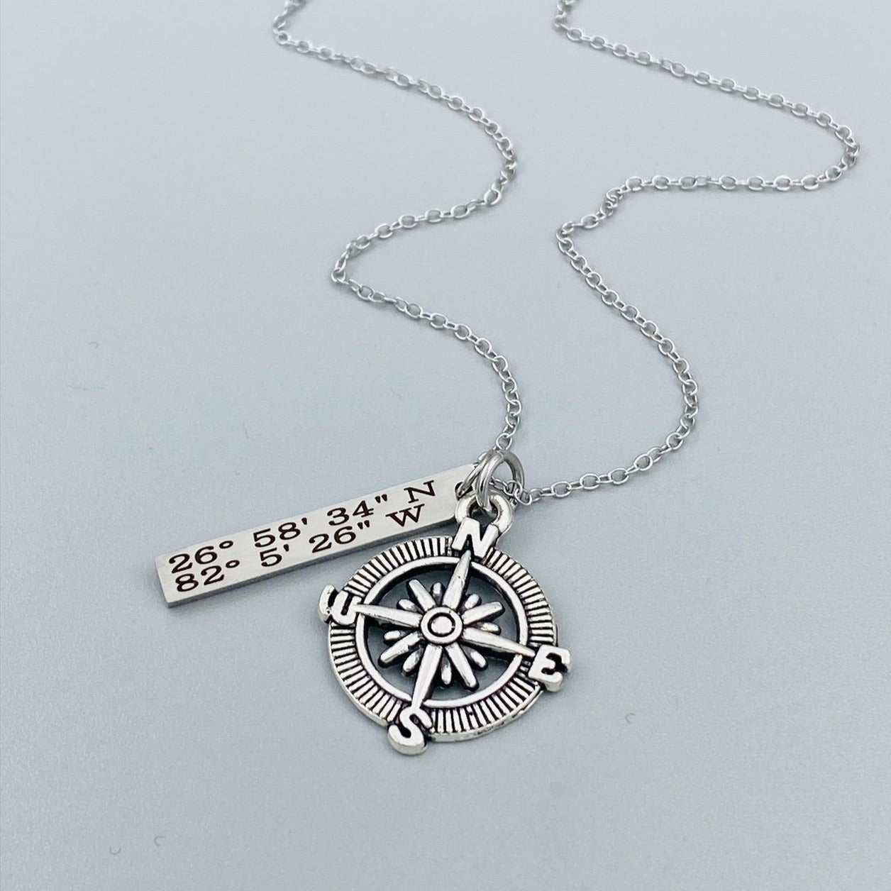 A silver compass necklace with a stainless steel pendant with personalized latitude and longitude coordinates