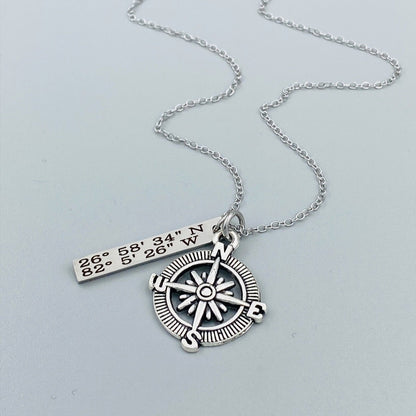 A silver compass necklace with a stainless steel pendant with personalized latitude and longitude coordinates