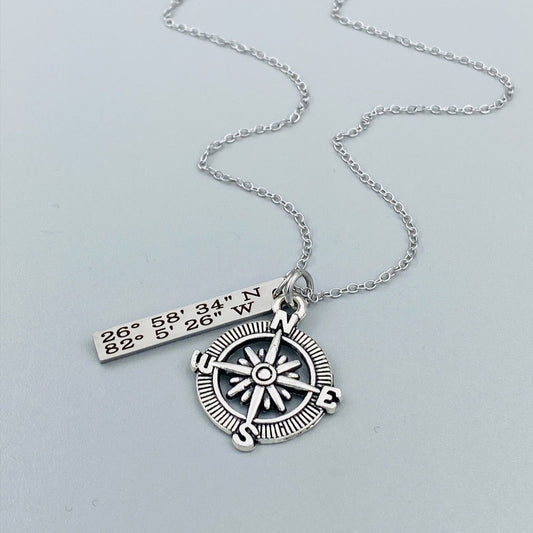 A silver compass necklace with a stainless steel pendant with personalized latitude and longitude coordinates