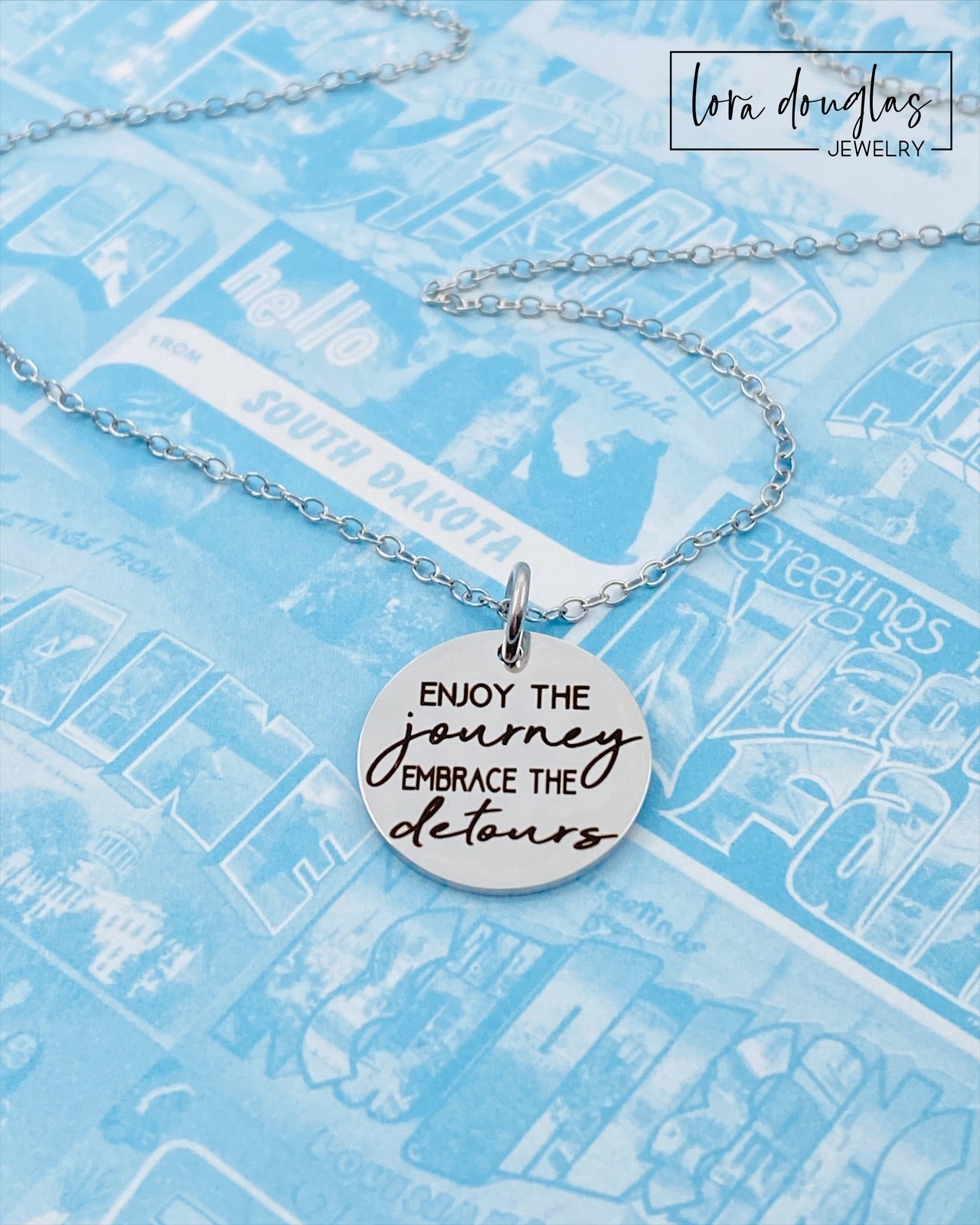 A silver necklace with a lobster clasp and a stainless steel bangle bracelet, both featuring an engraved message 'Enjoy the Journey, Embrace the Detours'