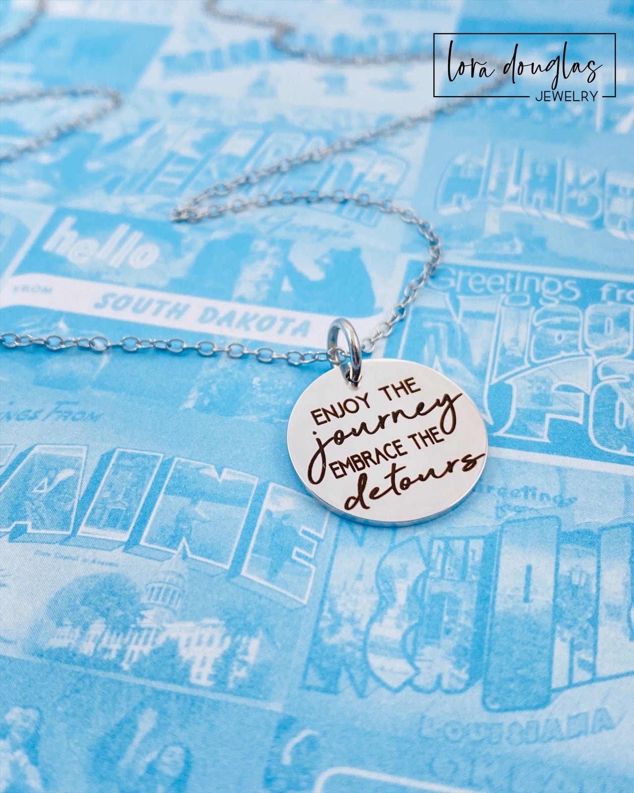 A silver necklace with a lobster clasp and a stainless steel bangle bracelet, both featuring an engraved message 'Enjoy the Journey, Embrace the Detours'