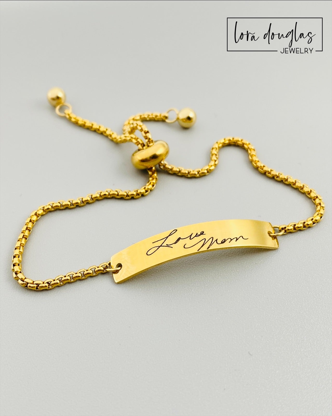A gold bracelet with a bar pendant engraved with the handwritten message 