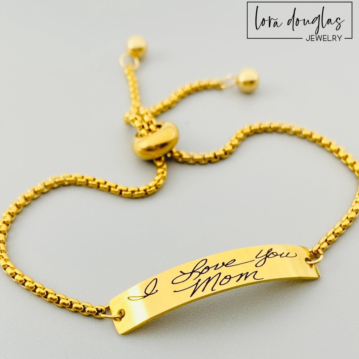 A gold bracelet with a bar pendant engraved with a handwritten message 