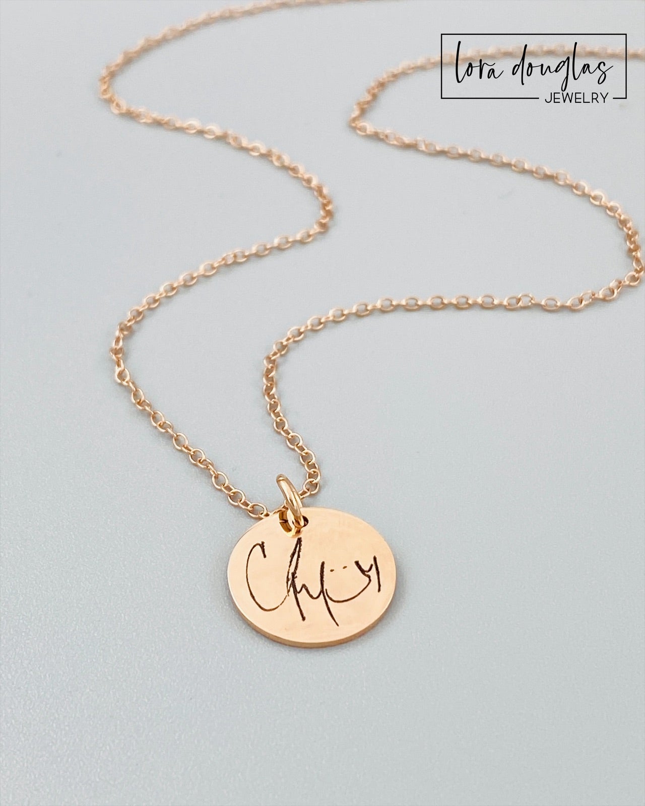 rose gold engraved necklaces displayed on a white background. necklace has a personalized handwritten message engraved on a disc charm, with varying text colors and styles.