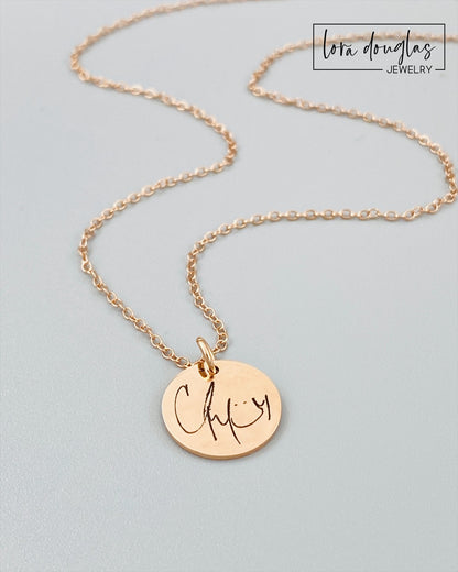 rose gold engraved necklaces displayed on a white background. necklace has a personalized handwritten message engraved on a disc charm, with varying text colors and styles.