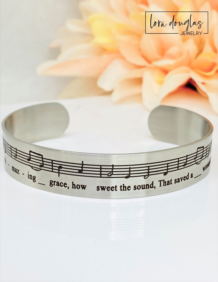 Celebrate the timeless beauty of "Amazing Grace" with this elegant sheet music bracelet. Featuring a delicate 1/2" width band engraved with the song’s iconic notes, it’s a meaningful gift for musicians, choir members, or anyone touched by this classic hymn. Perfect for recitals, piano players, or music lovers, this bracelet combines style and sentiment in a wearable keepsake. Give a gift that speaks to the heart and honors the power of music.