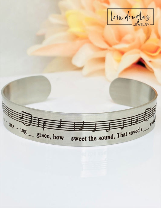 Celebrate the timeless beauty of "Amazing Grace" with this elegant sheet music bracelet. Featuring a delicate 1/2" width band engraved with the song’s iconic notes, it’s a meaningful gift for musicians, choir members, or anyone touched by this classic hymn. Perfect for recitals, piano players, or music lovers, this bracelet combines style and sentiment in a wearable keepsake. Give a gift that speaks to the heart and honors the power of music.