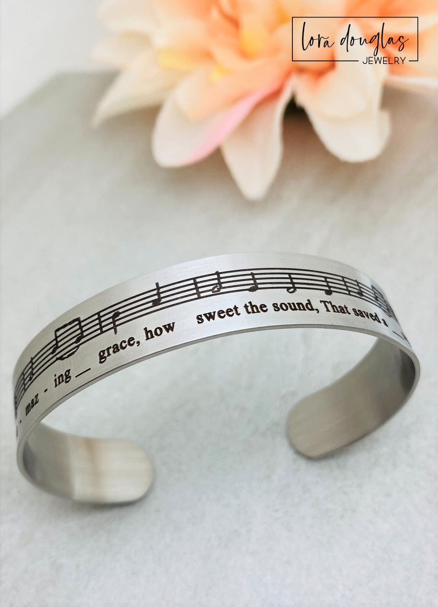 Celebrate the timeless beauty of "Amazing Grace" with this elegant sheet music bracelet. Featuring a delicate 1/2" width band engraved with the song’s iconic notes, it’s a meaningful gift for musicians, choir members, or anyone touched by this classic hymn. Perfect for recitals, piano players, or music lovers, this bracelet combines style and sentiment in a wearable keepsake. Give a gift that speaks to the heart and honors the power of music.