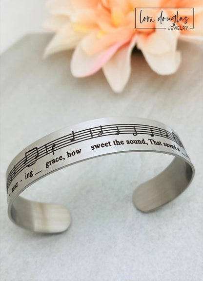 Celebrate the timeless beauty of "Amazing Grace" with this elegant sheet music bracelet. Featuring a delicate 1/2" width band engraved with the song’s iconic notes, it’s a meaningful gift for musicians, choir members, or anyone touched by this classic hymn. Perfect for recitals, piano players, or music lovers, this bracelet combines style and sentiment in a wearable keepsake. Give a gift that speaks to the heart and honors the power of music.