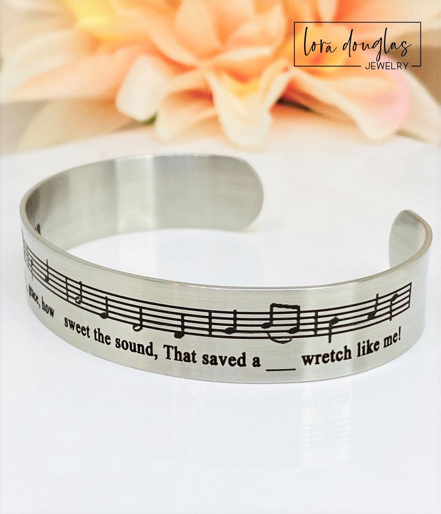 Celebrate the timeless beauty of "Amazing Grace" with this elegant sheet music bracelet. Featuring a delicate 1/2" width band engraved with the song’s iconic notes, it’s a meaningful gift for musicians, choir members, or anyone touched by this classic hymn. Perfect for recitals, piano players, or music lovers, this bracelet combines style and sentiment in a wearable keepsake. Give a gift that speaks to the heart and honors the power of music.