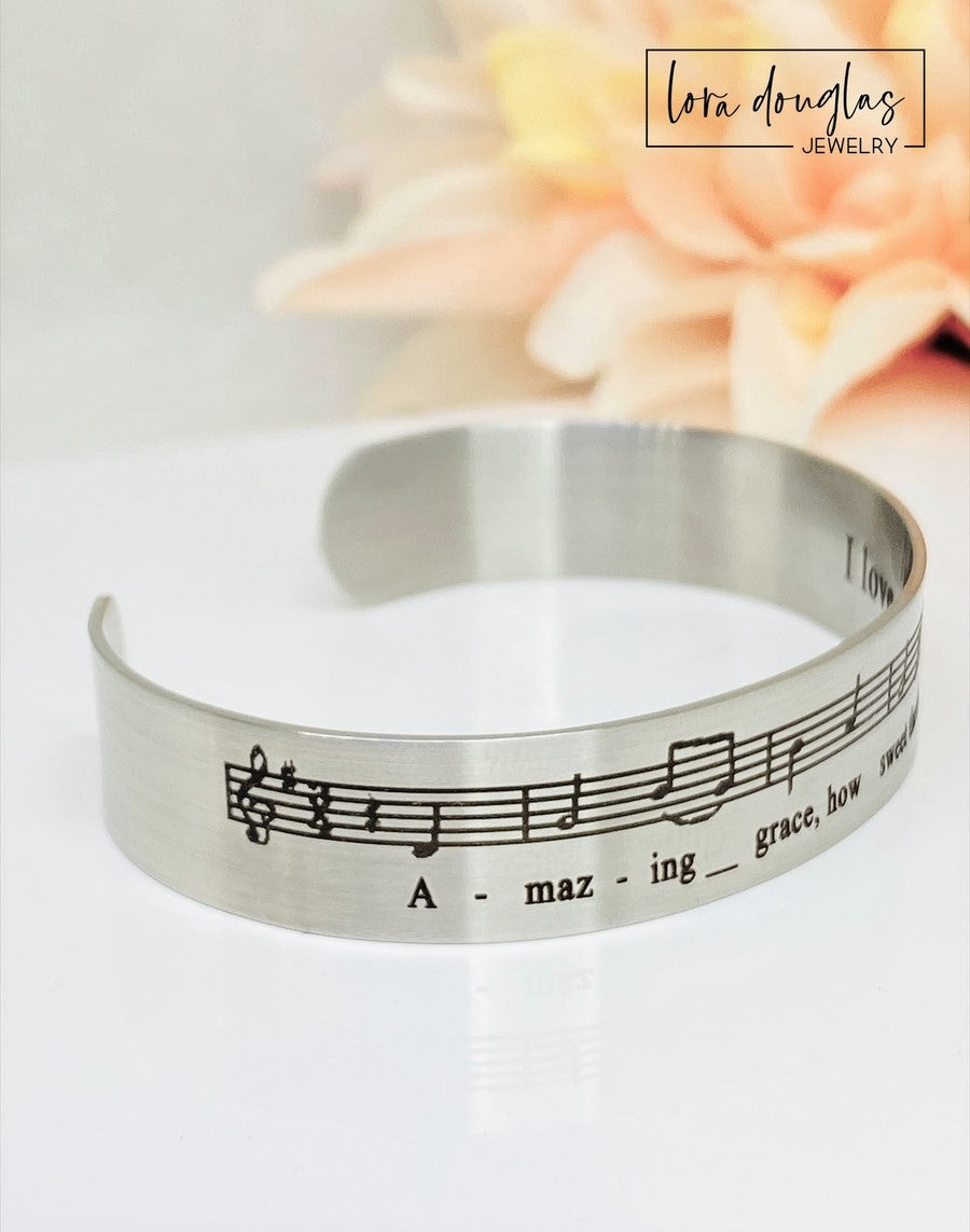 Celebrate the timeless beauty of "Amazing Grace" with this elegant sheet music bracelet. Featuring a delicate 1/2" width band engraved with the song’s iconic notes, it’s a meaningful gift for musicians, choir members, or anyone touched by this classic hymn. Perfect for recitals, piano players, or music lovers, this bracelet combines style and sentiment in a wearable keepsake. Give a gift that speaks to the heart and honors the power of music.