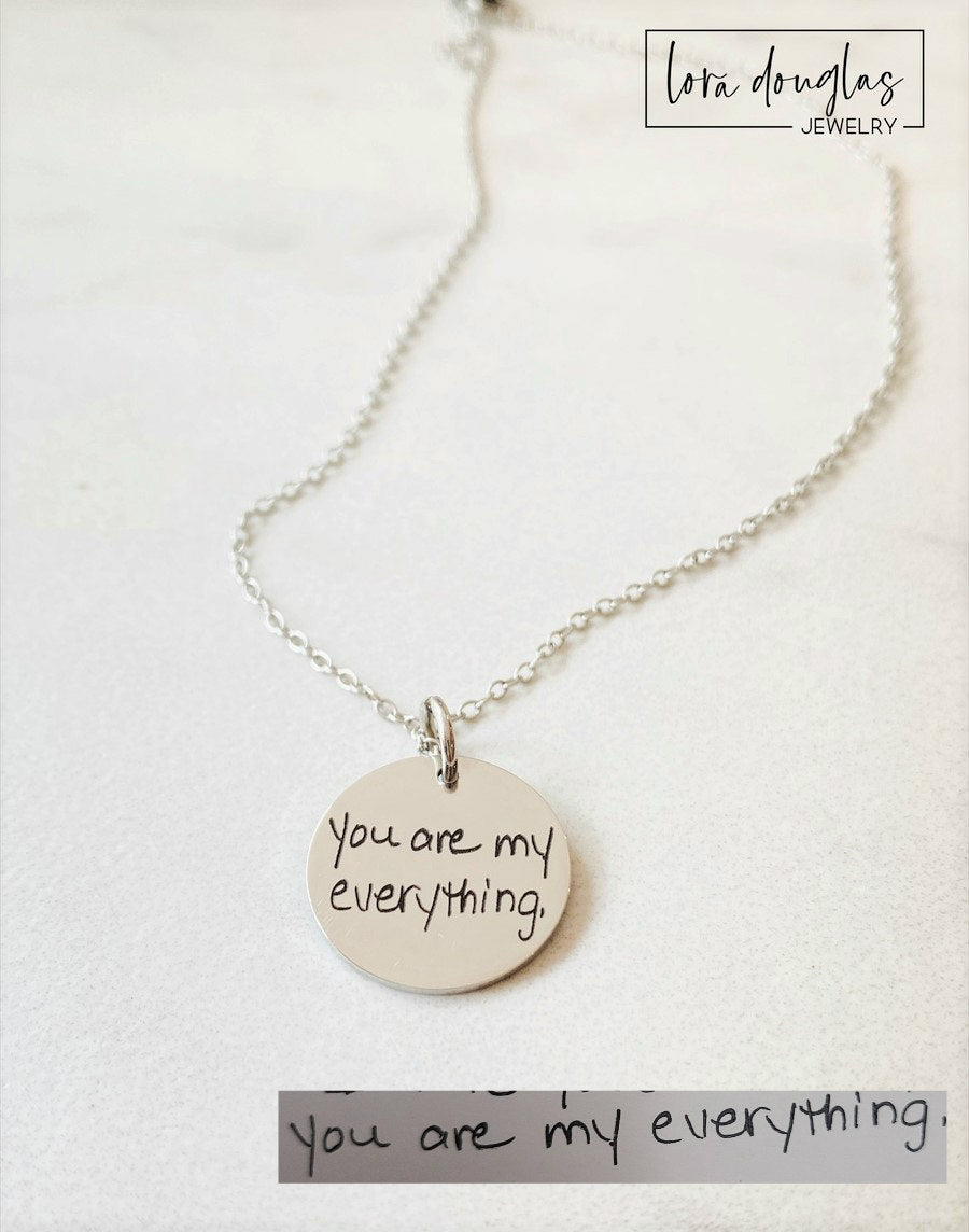 A round silver pendant with engraved with handwritten text 