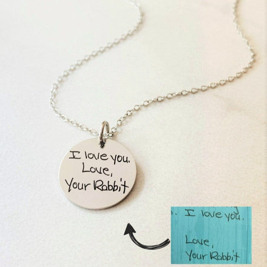 A round silver pendant with engraved with handwritten text that reads 'I love you, your rabbit.'