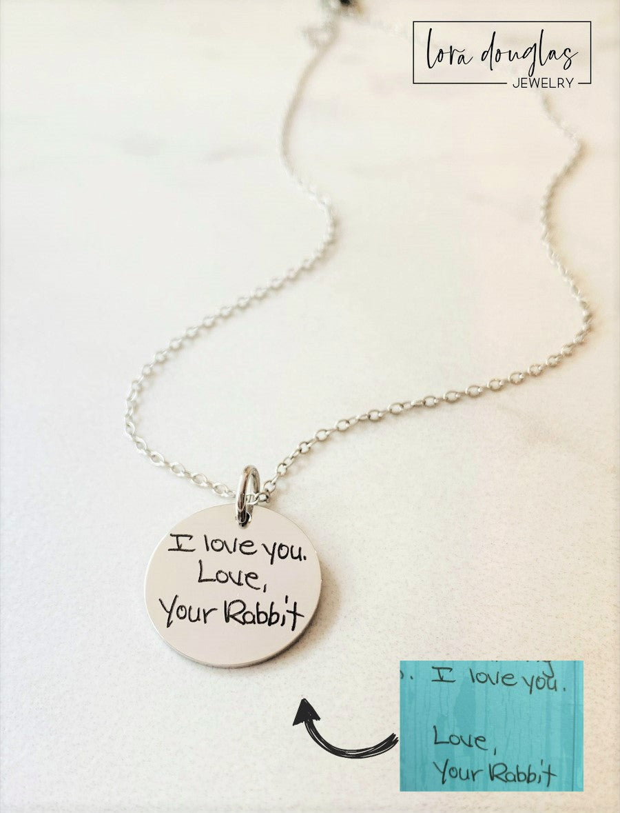 silver engraved necklaces displayed on a white background. Each necklace has a personalized handwritten message engraved on a disc charm, with varying text colors and styles.