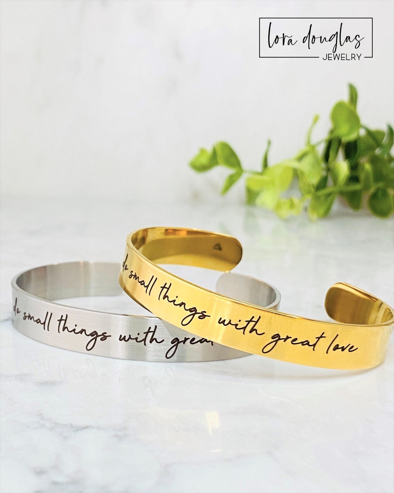 Two stainless steel cuff bracelets, one in silver and one in gold color, each with an engraved message 'Do small things with great love'.