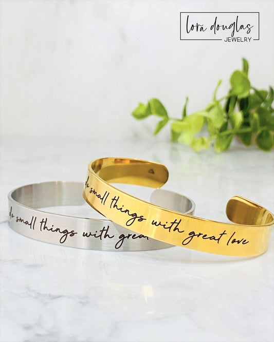 Two stainless steel cuff bracelets, one in silver and one in gold color, each with an engraved message 'Do small things with great love'.