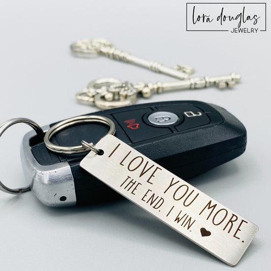 A stainless steel metal keychain with the engraved text 'I Love You More. The End. I Win.' 