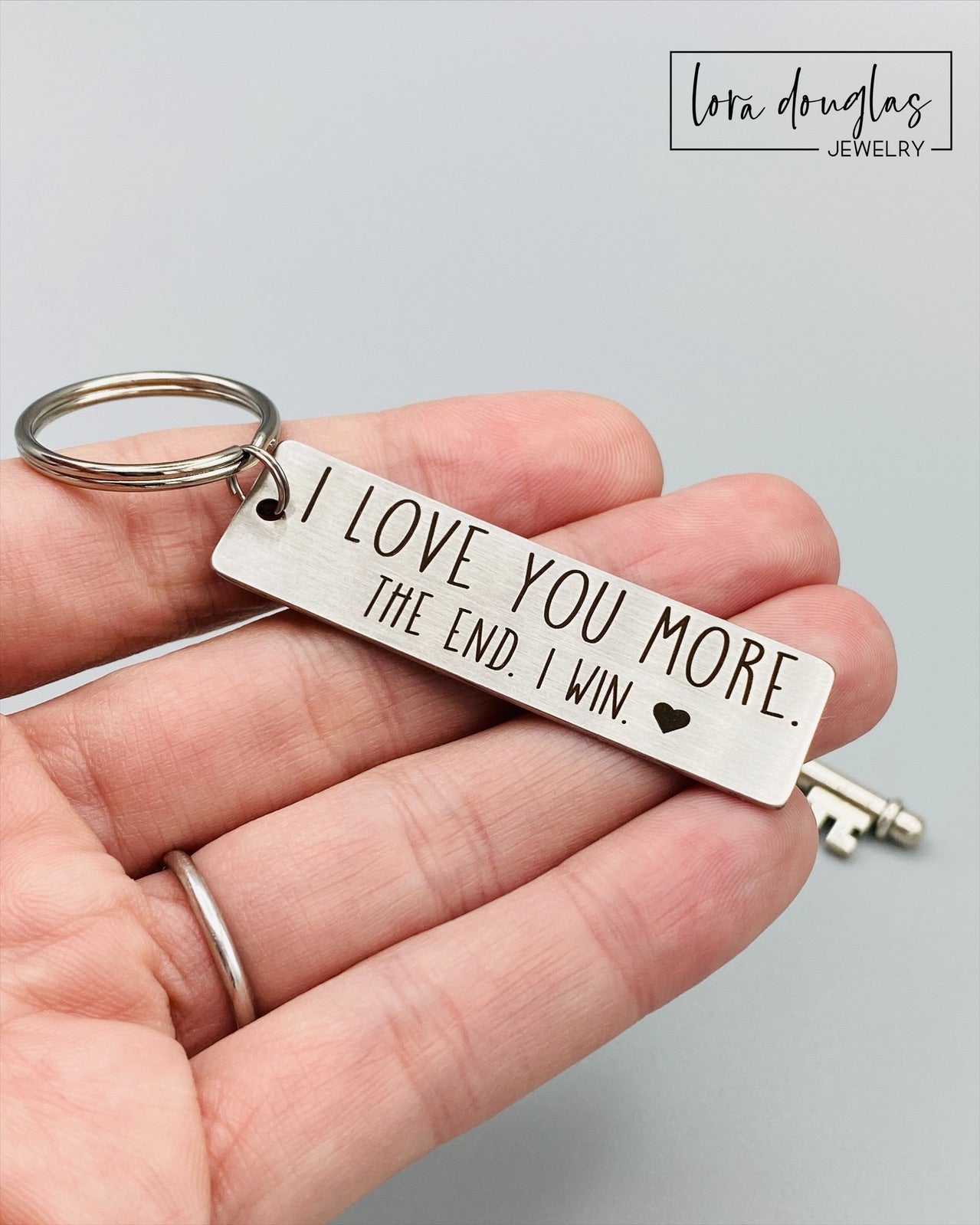 A stainless steel metal keychain with the engraved text 'I Love You More. The End. I Win.' 