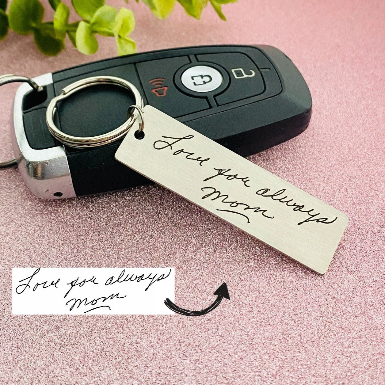 A stainless steel keychain with laser engraved handwriting on it, placed on a car key. 